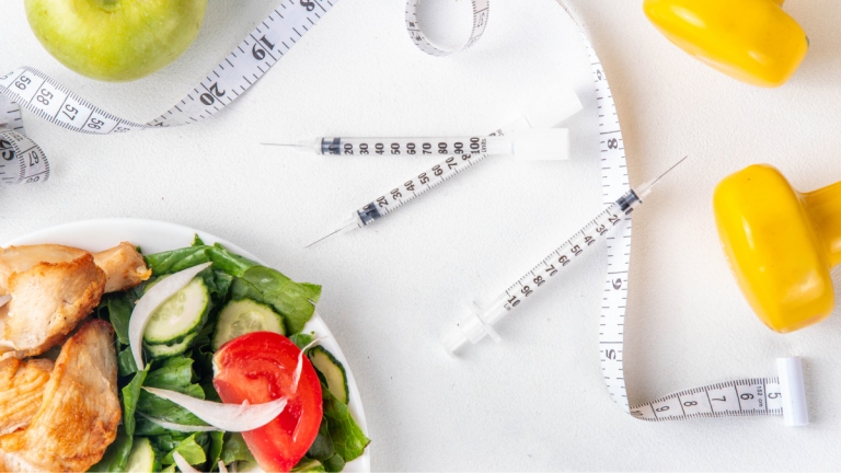 needles for weight loss injections are arranged on a table with a healthy dinner, apples, dumbells, and a tape measure